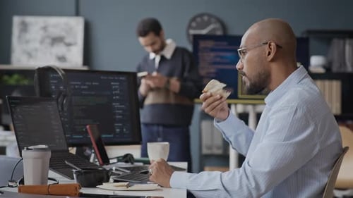 Indian Male IT Developer Eating Snack and Checking Phone during Office Break