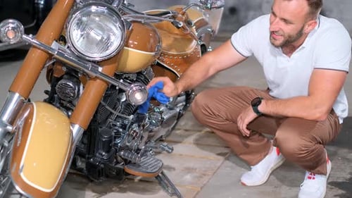 A Young Man in a Garage Near a Motorcycle He Rubs the Chrome Engine Until It Shines