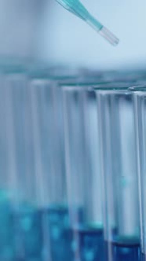 Close-up of Drops of Blue Solution Falling from Pipette into Test Tubes