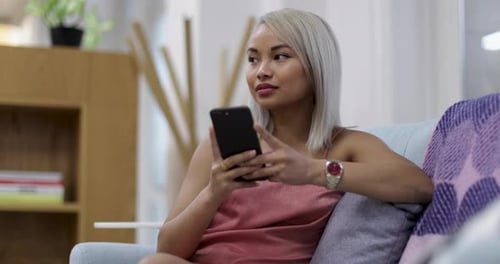Smiling woman using mobile phone while sitting on sofa