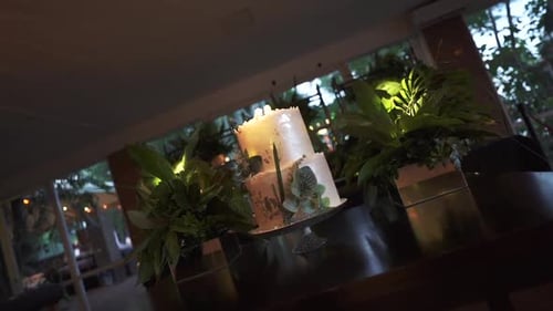 Elegant wedding cake adorned with flowers and greenery in a dimly lit reception hall