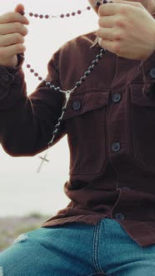 Man Holding A Rosary In His Hands During A Prayer On The Beach