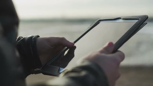 Männliche Hand, die das Tablet mit der Fingerspitze berührt, während es auf einem Tisch gehalten wird (geringe Schärfentiefe)