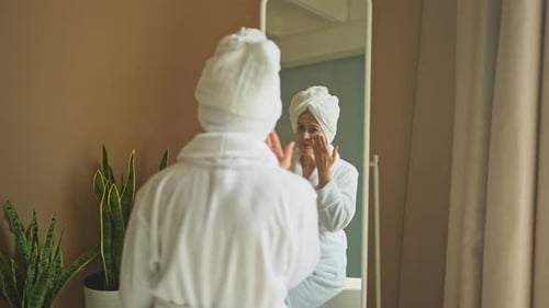 Woman in Robe Applies Lotion to Face