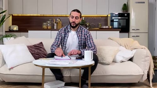 Man Calculates Finances at Home on Couch