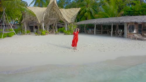 Beautiful Sexy Girl in a Red Dress Walking Down the White Sand Beach on a Paradise Tropical Island