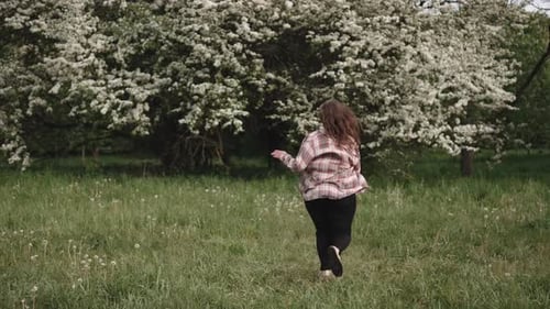 Frau in Übergröße im karierten Hemd rennt zum blühenden Baum — Rückansicht