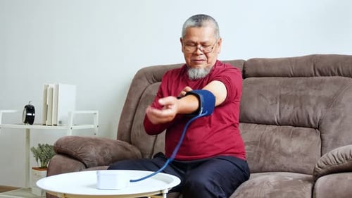 Senior Man Checking Blood Pressure at Home on Sofa