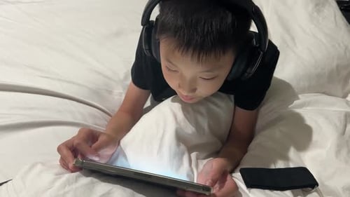 Child With Headphones Using Tablet on Bed