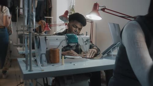 Young Adult Tailor Sewing in Bright Workshop