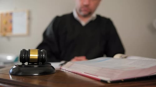 Die Hand des Richters mit dem hölzernen Richter Gavel und schreibt seine Entscheidung nieder. Fokus auf Richter Gavel (Zeitlupe)