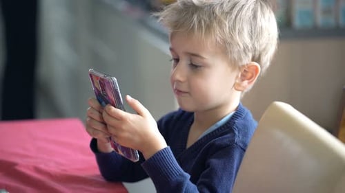 Young Boy Concentrating on Mobile Phone at Table