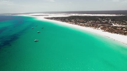 Aerial view of a serene beach with turquoise water and fishing boats near a coastal town
