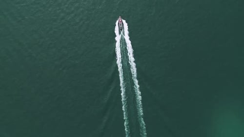 Overhead view footage of a boat sailing across calm blue water on a sunny day, creating ripples and