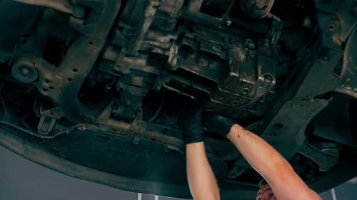 Close Up an Auto Mechanic at Service Station Checks a Car Being Lifted on a Lift Fixing Problems