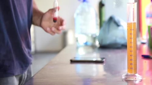 Primer plano de un hombre probando el porcentaje original de gravedad/alcohol de la cerveza en un hidrómetro