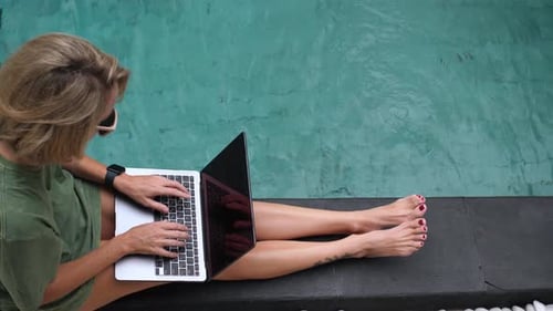Mid Adult Woman Sitting at the Poolside Using Laptop