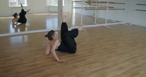 Mädchen im schwarzen Anzug liegt auf Holzboden und führt während ihres Choreografiekonzepts Beinbewegungen aus