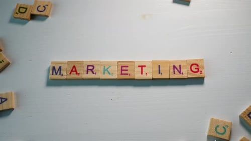 A table with scattered wooden letters and a person spelling Marketing. White background. Dramatic li