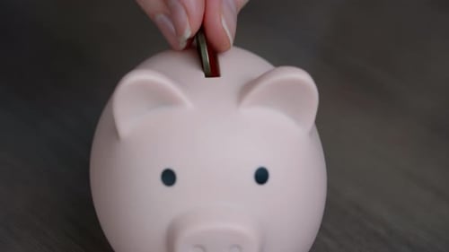 Vue de dessus des mains d'une femme mettant de l'argent dans une tirelire.