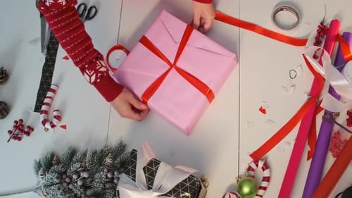 Caja de regalo envuelta con manos femeninas con lazo rojo, junto a elementos decorativos, bayas, tijeras, ramas de abeto
