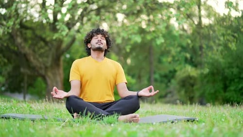 Young sports man meditating barefoot in the lotus position on a mat in an urban city park. Handsome