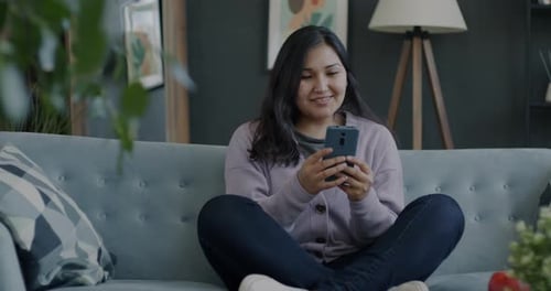 Woman Smiling and Using Cellphone Indoors on Couch