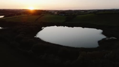 Orbit aerial view of lake in front of sunset in scenic countryside