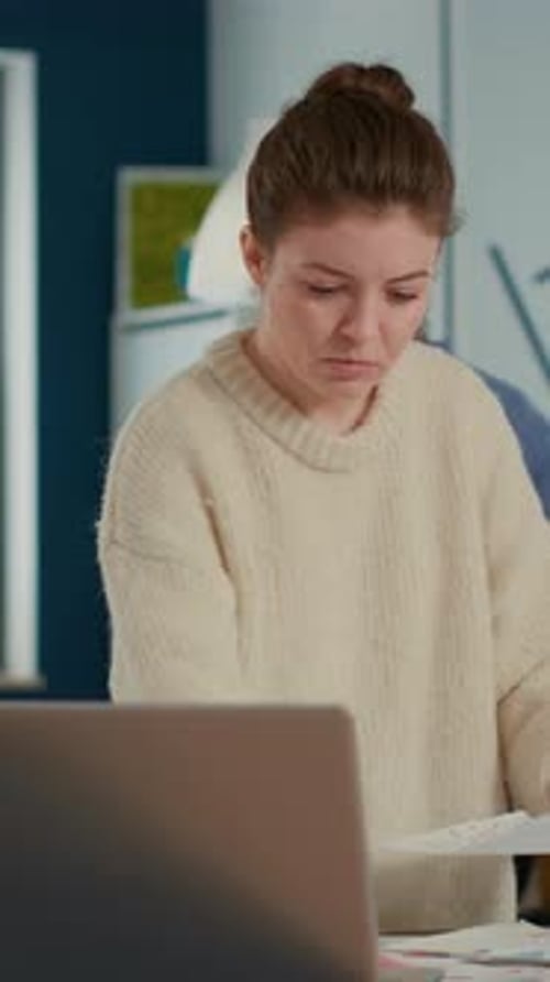 Portrait of Focused Startup Employee Looking at Laptop and Charts Comparing Sales Statistics