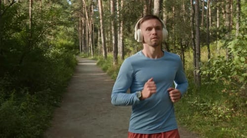 Young Man Listening to Music While Jogging in Forest on Sunny Day