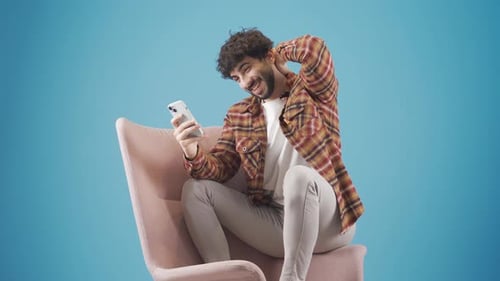 Lässig gekleideter junger Mann, der zu Hause mit dem Smartphone eine SMS schreibt.