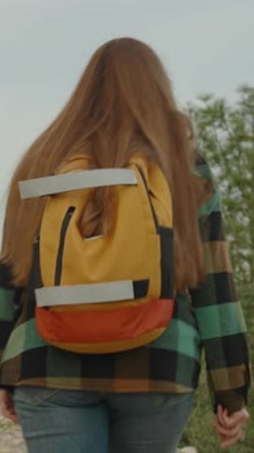 Vertical video. Ascent to the mountain, a woman with a bright backpack approaches the edge.