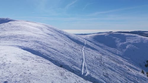 Drone view of snowy mountains and peaceful winter trail under blue sky