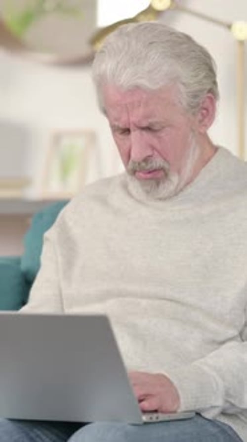 Senior Man Coughing While Using a Laptop Indoors