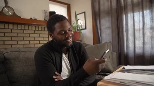 Black man texting on phone smiling in living room medium shot