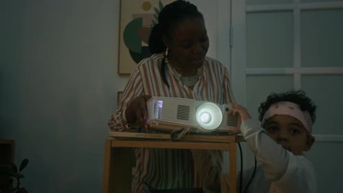 Woman and Child Using Projector Indoors at Night