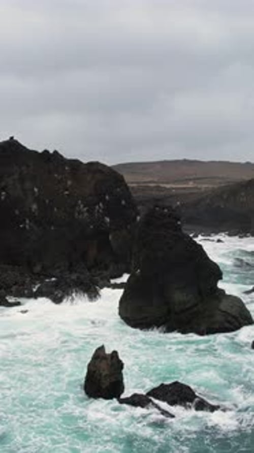 Valahnukamol: Powerful turquoise ocean waves crashing against dramatic black volcanic cliffs
