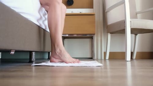 female feet standing on the floor rug from the bed after waking up
