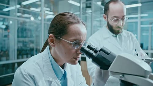 Female Scientist Conducting Microscopic Research with Assistant in Laboratory