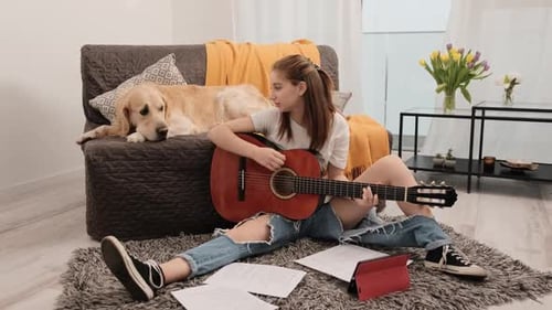 Young Woman Plays Guitar with Dog Nearby