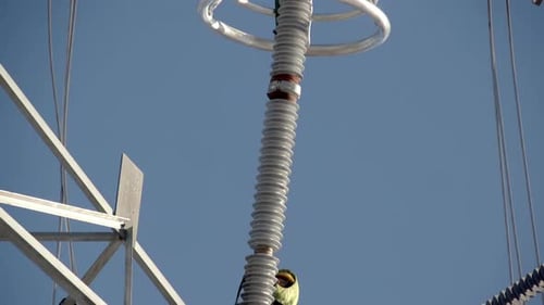 Tilt-down Reveal Of Linemen Working On Insulation String Of Transmission Tower. low angle