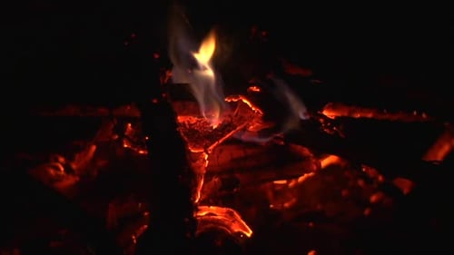 Fan winds blowing on coals of small camp fire causing small embers of to glow brightly and break awa