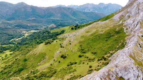 Slope of the high mountain covered with grass and bushes. Drone footage above the rock ridge.