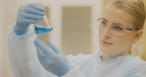Woman in Lab Coat Examines Beaker of Blue Liquid