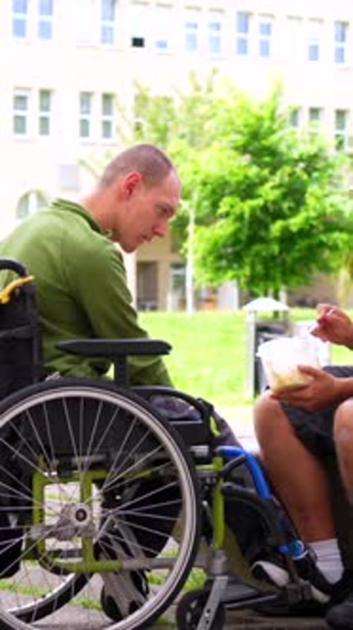 Amigo alimentando um homem com deficiência fora do campus universitário