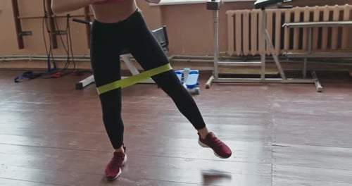 Young Woman Working Out with Elastic Sport Straps or Bands Doing Leg Exercises in a Gym in a Low