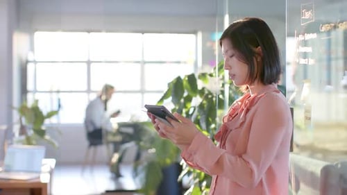 Thoughtful asian businesswoman using tablet at sunny office, copy space, in slow motion