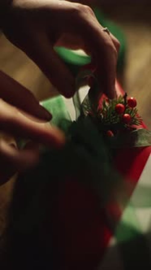 Hands Decorating Festive Christmas Gift with Berries and Ribbon