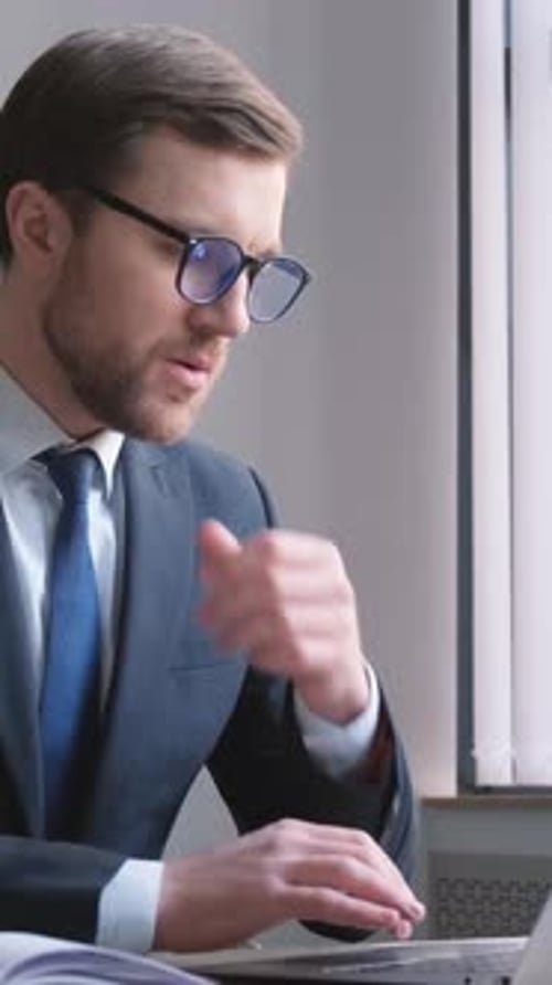 A Professional in a Suit Works Diligently at His Office Desk with a Laptop