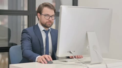 Young Businessman Smiling at Camera while Working on Computer